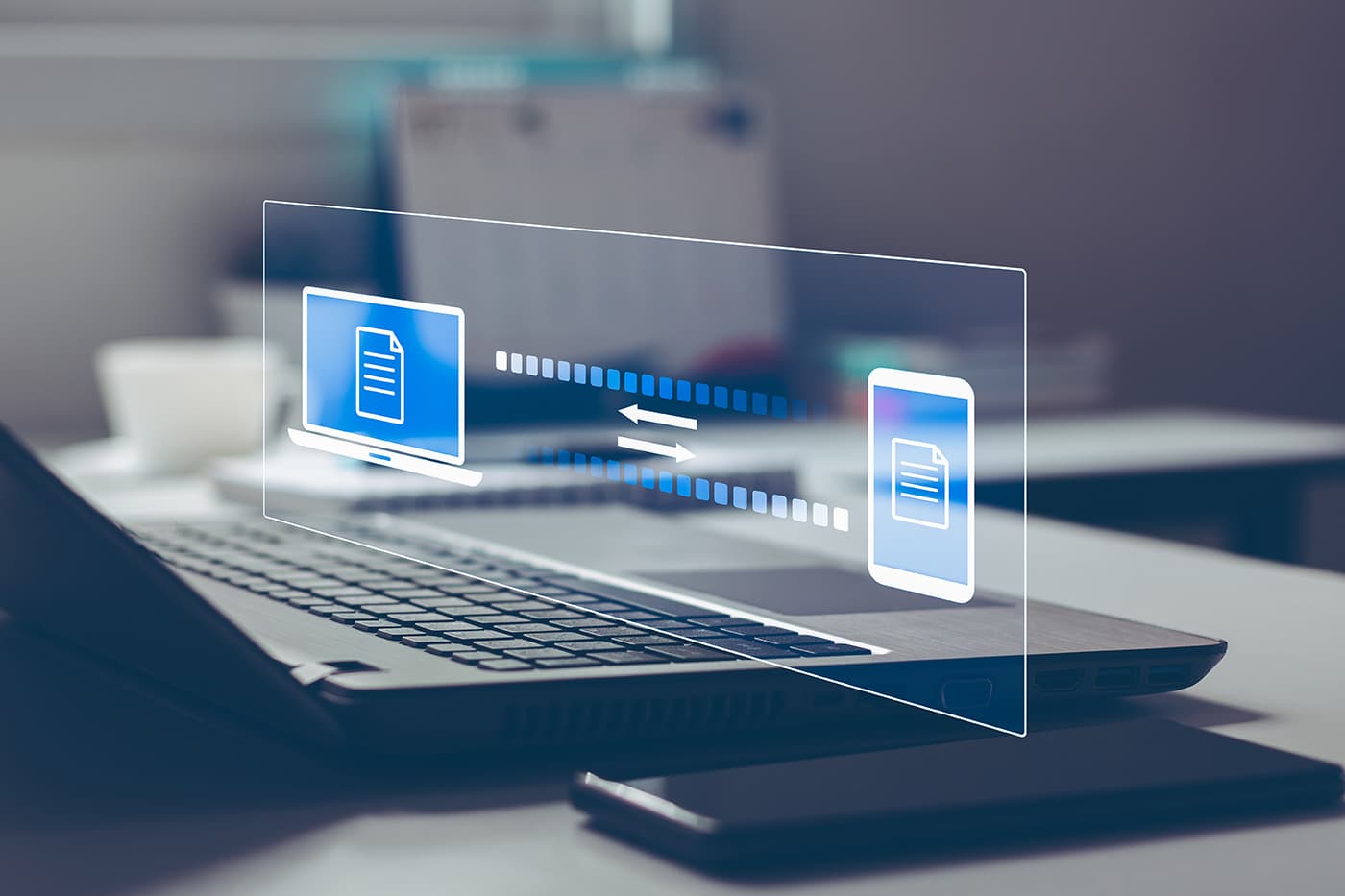 A laptop displaying a holographic illustration of documents transferring between a computer and a mobile device